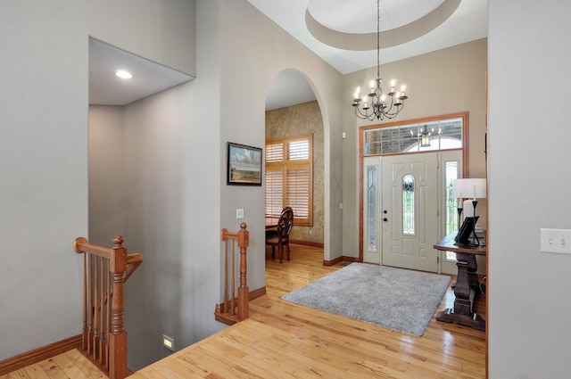 entrance foyer featuring arched walkways, a chandelier, hardwood / wood-style floors, baseboards, and a high ceiling
