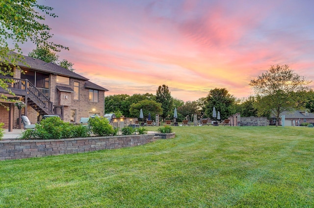 yard at dusk with a patio area, a lawn, stairway, and a sunroom