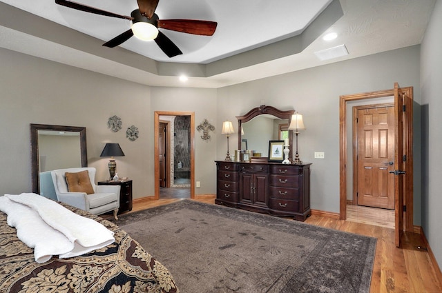 bedroom featuring light wood-type flooring, baseboards, ceiling fan, and a tray ceiling