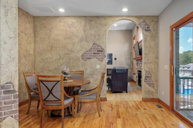 dining area with hardwood / wood-style flooring, a fireplace, healthy amount of natural light, arched walkways, and recessed lighting