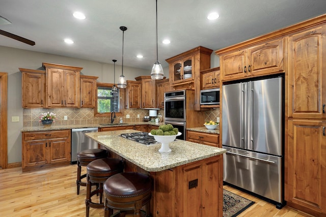 kitchen featuring appliances with stainless steel finishes, a sink, brown cabinets, light wood-style floors, and recessed lighting