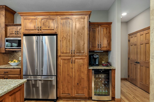 kitchen with stainless steel appliances, wine cooler, tasteful backsplash, light wood-style floors, and light stone countertops