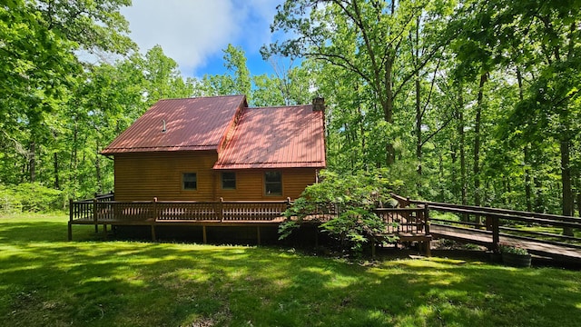 view of property exterior with a wooden deck, a yard, a chimney, and metal roof