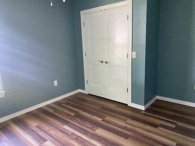 unfurnished bedroom with baseboards, dark wood-style floors, and a closet