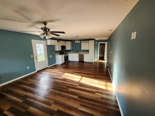 unfurnished living room with dark wood-style flooring, a ceiling fan, and baseboards
