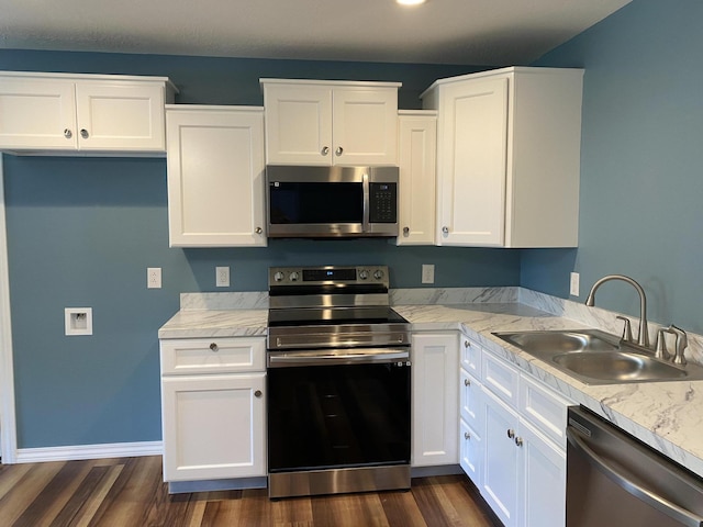 kitchen with appliances with stainless steel finishes, a sink, dark wood finished floors, and white cabinets