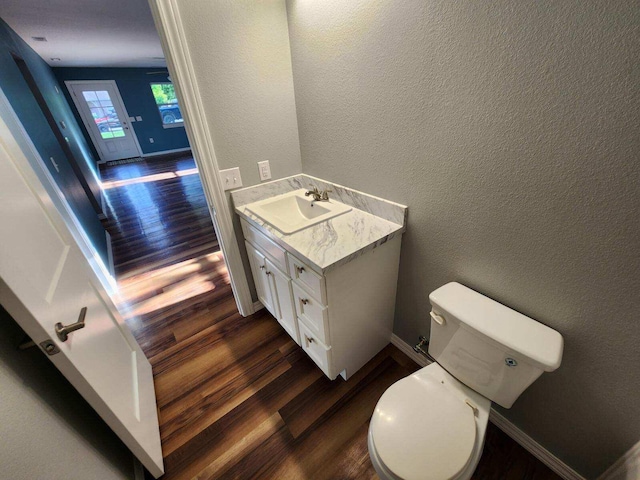 half bath featuring wood finished floors, toilet, vanity, and a textured wall