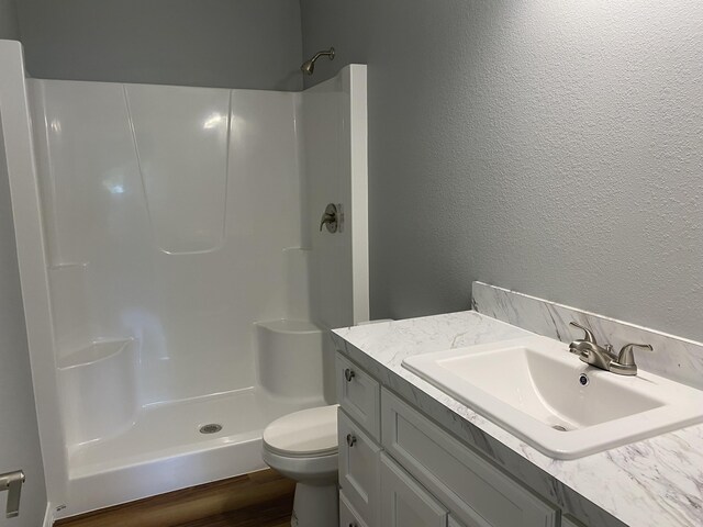 bathroom with a textured wall, a shower, toilet, and vanity