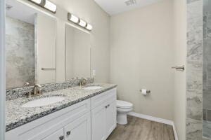 full bath with toilet, wood finished floors, double vanity, baseboards, and a shower