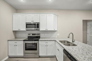 kitchen featuring appliances with stainless steel finishes, a sink, white cabinets, a peninsula, and tasteful backsplash