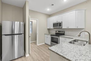 kitchen featuring appliances with stainless steel finishes, a sink, light stone countertops, light wood-style flooring, and white cabinets