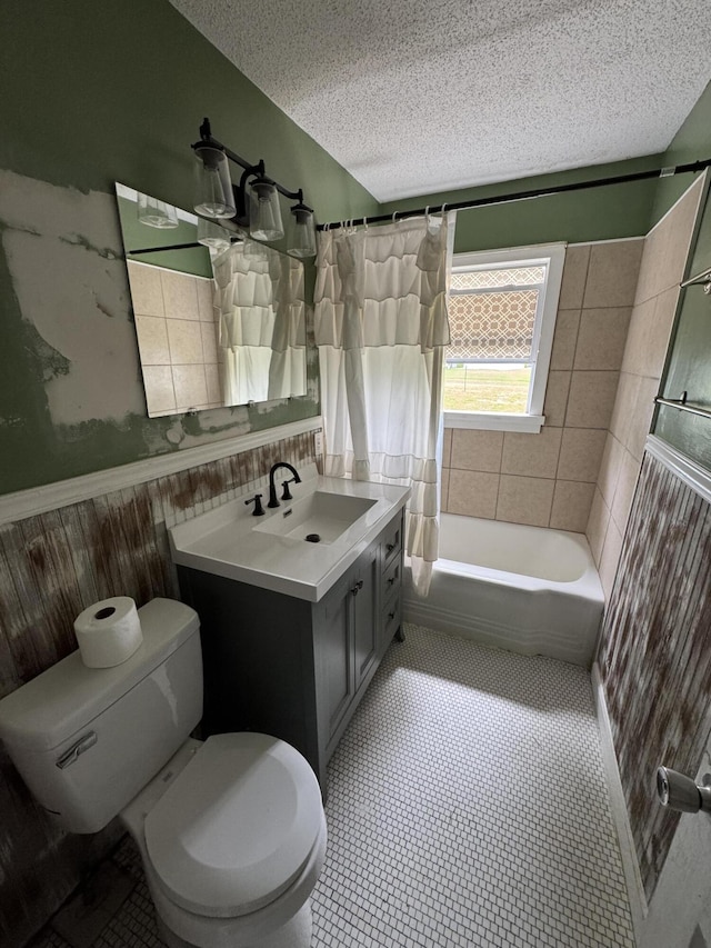 bathroom featuring toilet, a textured ceiling, vanity, a wainscoted wall, and shower / tub combo