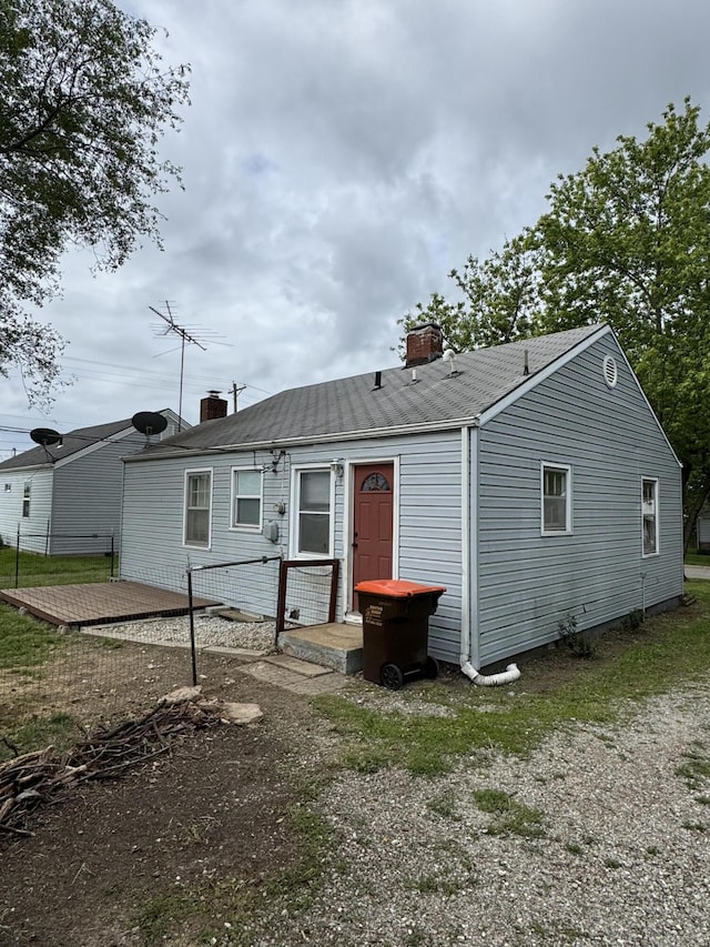 back of house with a chimney and a shingled roof