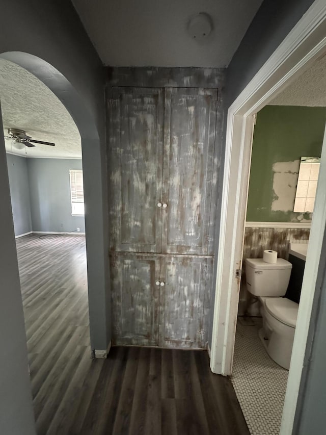 bathroom featuring toilet, a textured ceiling, wood finished floors, ceiling fan, and wainscoting