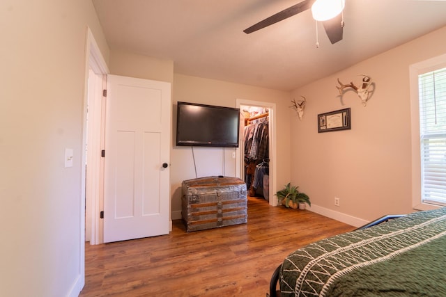 bedroom with wood finished floors, baseboards, a spacious closet, a closet, and a ceiling fan