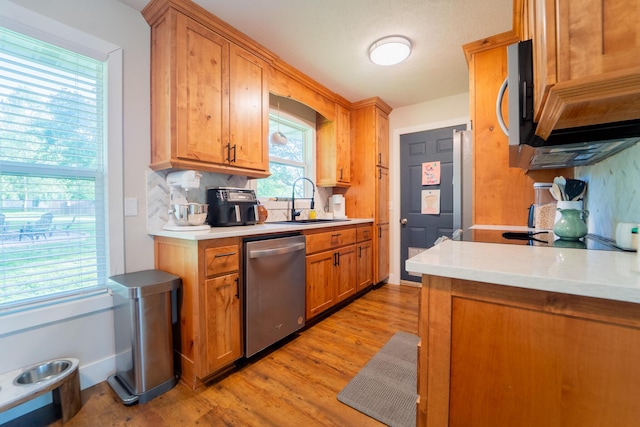kitchen with stainless steel appliances, a sink, decorative backsplash, light wood-type flooring, and light countertops