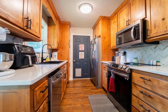 kitchen with stainless steel appliances, a sink, backsplash, brown cabinetry, and a textured ceiling