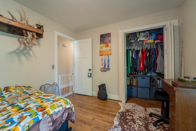 bedroom with wood finished floors, a desk, baseboards, and a closet