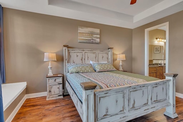 bedroom featuring wood finished floors, baseboards, and a raised ceiling