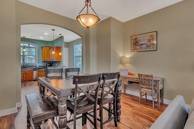dining space with arched walkways, baseboards, and light wood-type flooring
