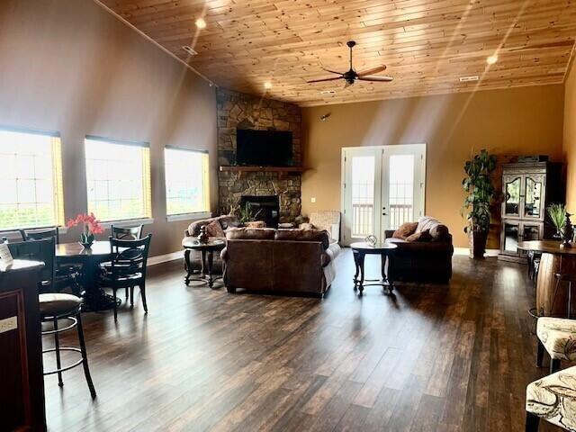 living room featuring ceiling fan, wooden ceiling, dark wood-style floors, a stone fireplace, and plenty of natural light