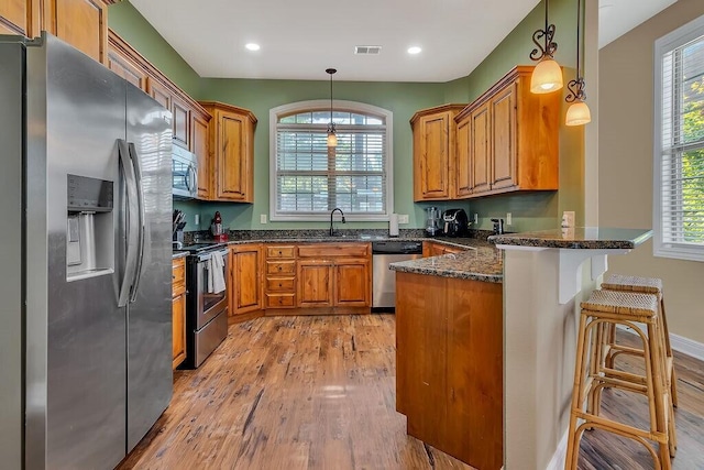 kitchen featuring stainless steel appliances, a peninsula, light wood finished floors, brown cabinets, and recessed lighting