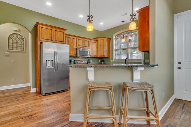 kitchen featuring appliances with stainless steel finishes, a breakfast bar area, light wood-type flooring, pendant lighting, and baseboards