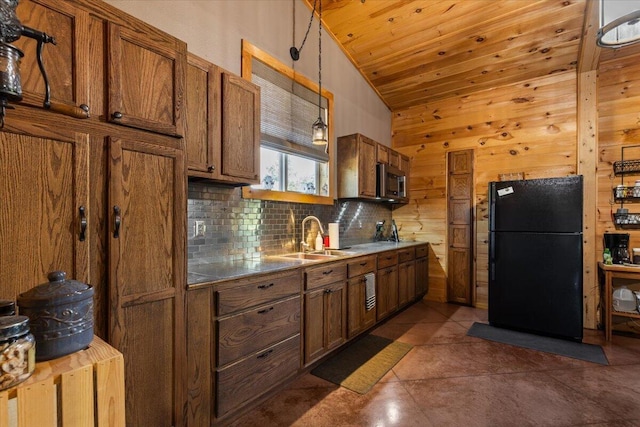kitchen with freestanding refrigerator, stainless steel microwave, a sink, brown cabinets, and vaulted ceiling