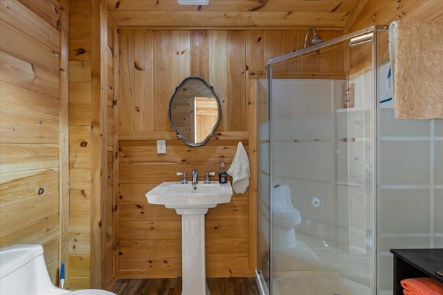 bathroom featuring a shower stall, toilet, wood walls, and wood finished floors