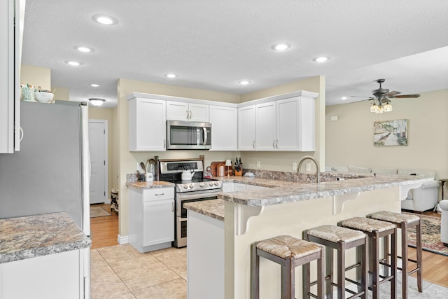 kitchen with appliances with stainless steel finishes, a breakfast bar area, a peninsula, recessed lighting, and a ceiling fan