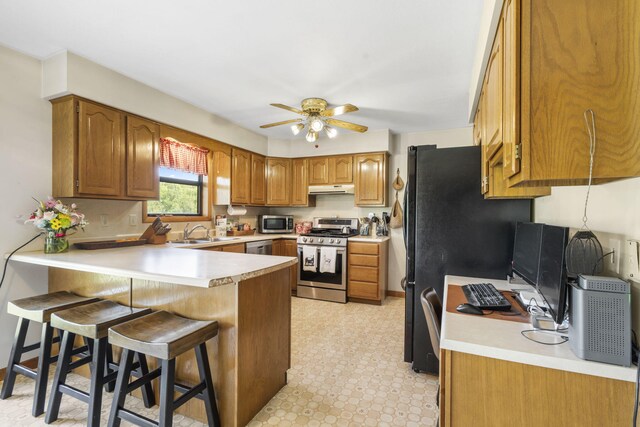 1065 Nicks Rd, Bradleyville, MO 65614 - kitchen with stainless steel appliances, a peninsula, under cabinet range hood, a ceiling fan, and a kitchen breakfast bar