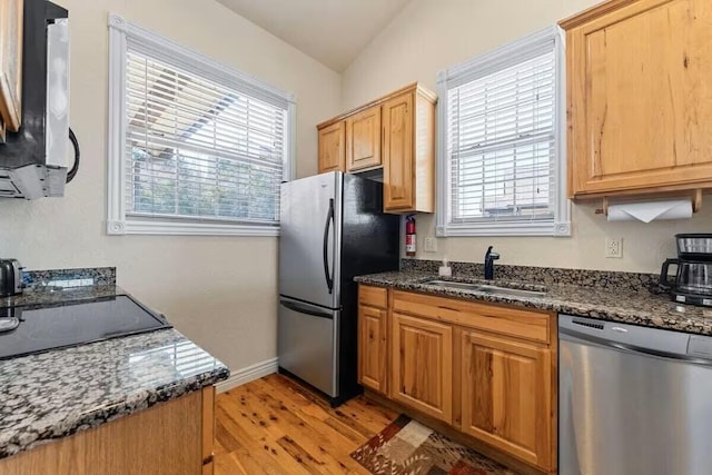 kitchen featuring appliances with stainless steel finishes, a sink, light wood-style floors, dark stone countertops, and baseboards