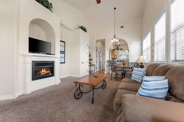 living room with a glass covered fireplace, carpet flooring, ceiling fan, baseboards, and vaulted ceiling