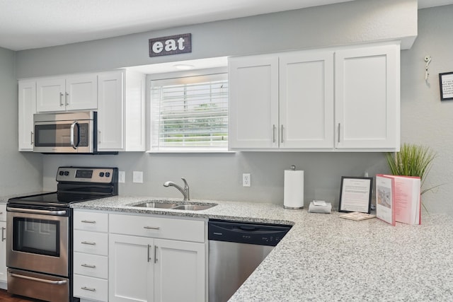 kitchen with stainless steel appliances, a sink, white cabinets, and light stone counters