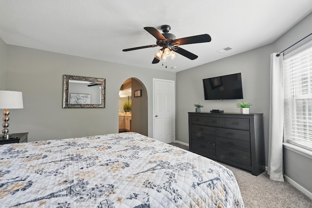 carpeted bedroom featuring arched walkways, baseboards, multiple windows, and a ceiling fan