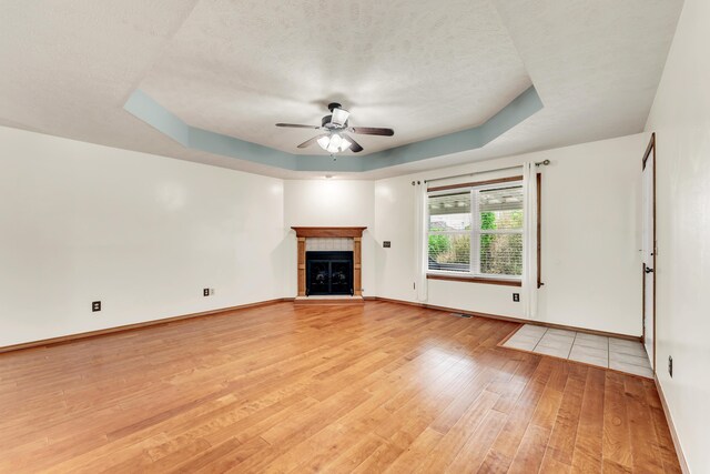 1240 Tyler Ln, Nixa, MO 65714 - unfurnished living room featuring a tray ceiling, light wood-type flooring, a ceiling fan, a tiled fireplace, and a textured ceiling