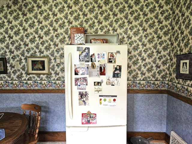 detailed view of freestanding refrigerator, wallpapered walls, and wainscoting