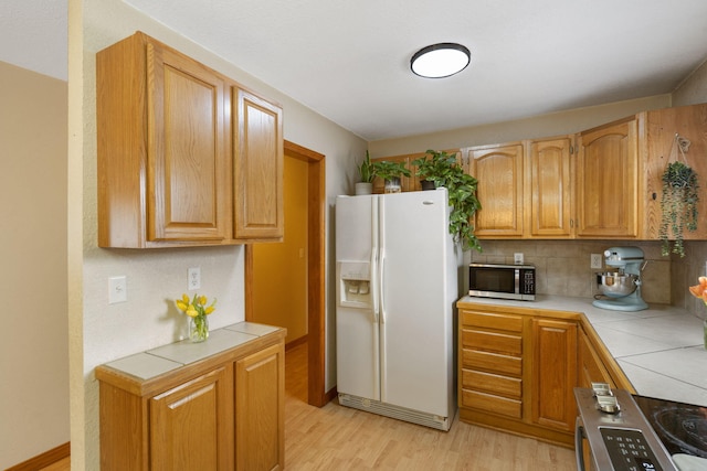 kitchen featuring appliances with stainless steel finishes, tile countertops, light wood finished floors, and decorative backsplash