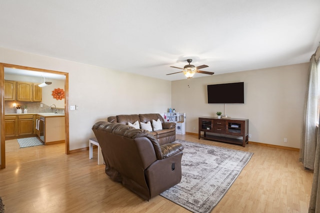 living area with light wood-type flooring, a ceiling fan, and baseboards