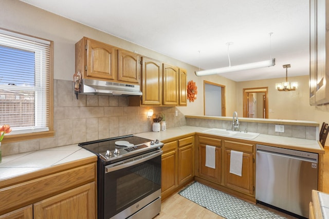 kitchen with stainless steel appliances, under cabinet range hood, a sink, tile counters, and decorative backsplash