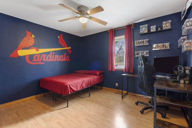 bedroom featuring wood finished floors, baseboards, an office area, and a ceiling fan
