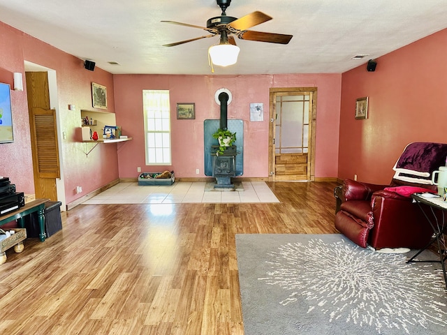 living room featuring a wood stove, wood finished floors, ceiling fan, and baseboards