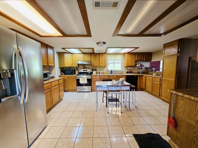 kitchen with stainless steel appliances, under cabinet range hood, light tile patterned floors, a sink, and light countertops