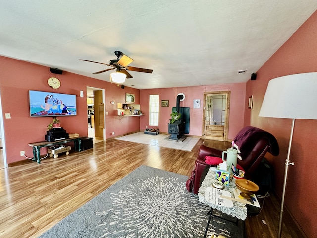 living area featuring a wood stove, wood finished floors, ceiling fan, and baseboards