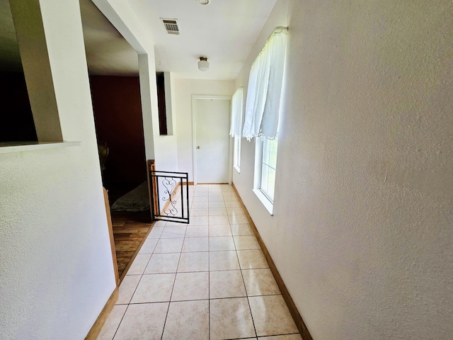 hall featuring a textured wall, baseboards, and light tile patterned flooring