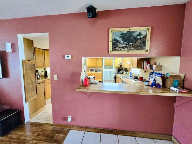 kitchen with washing machine and clothes dryer, a kitchen bar, a peninsula, light countertops, and a sink