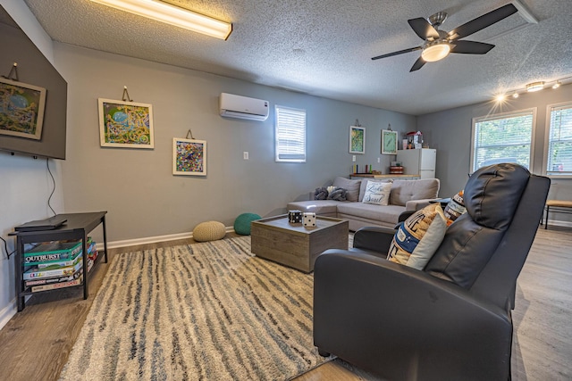 living area with a wall unit AC, light wood finished floors, ceiling fan, a textured ceiling, and baseboards