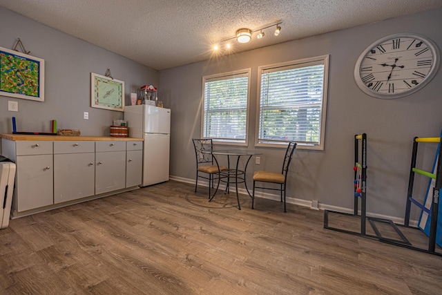kitchen with freestanding refrigerator, light wood-type flooring, a textured ceiling, white cabinetry, and baseboards