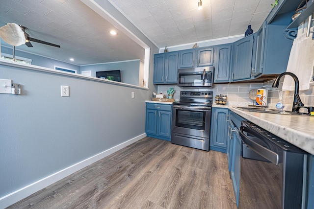 kitchen with appliances with stainless steel finishes, a sink, blue cabinetry, light countertops, and baseboards