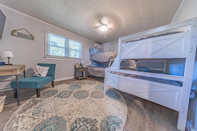 bedroom with ornamental molding, wood finished floors, a wall unit AC, baseboards, and a ceiling fan